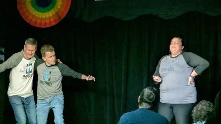 Three improvisers mid-scene in front of a green curtain