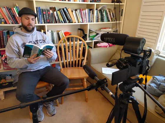 Man in a CATCh hoodie reading beside a camera on a tripod