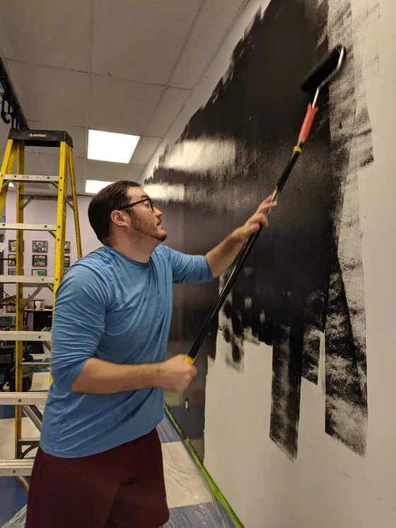 Volunteer painting a wall black with a roller