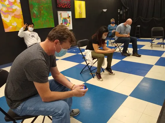 Masked improvisers seated far apart on the checkered stage floor
