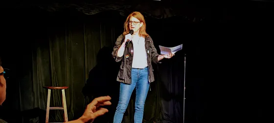 Performer reading from a page on a dark stage