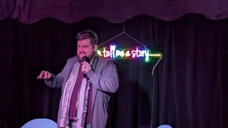 Storyteller at the microphone under a neon sign